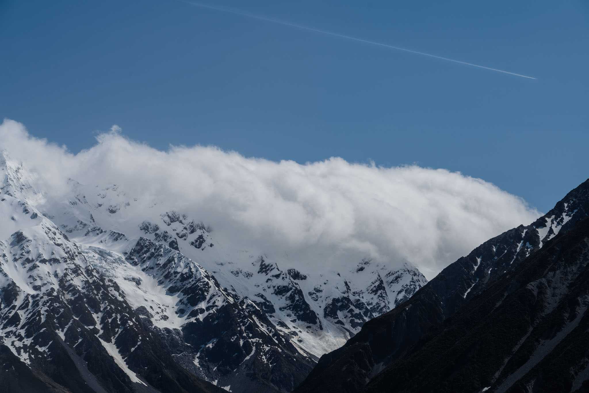Clouds with a plane crossing Mount Cook